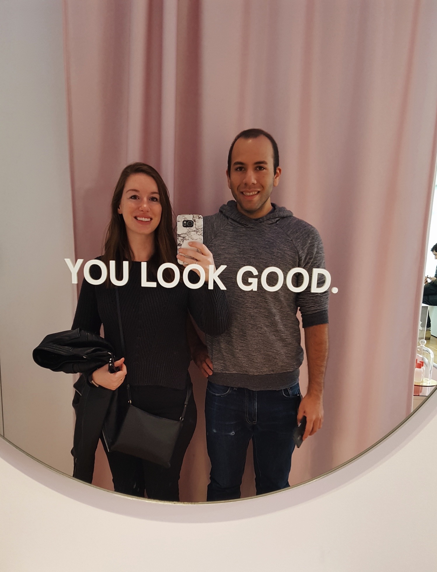 Alyssa and Michael take a photo in front of a mirror that reads You Look Good