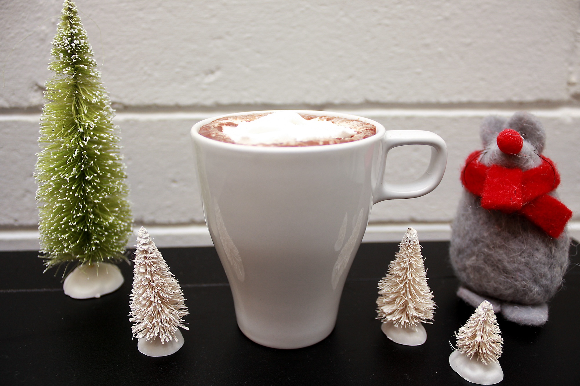 A mug with a marshmallow and little trees and a little mouse