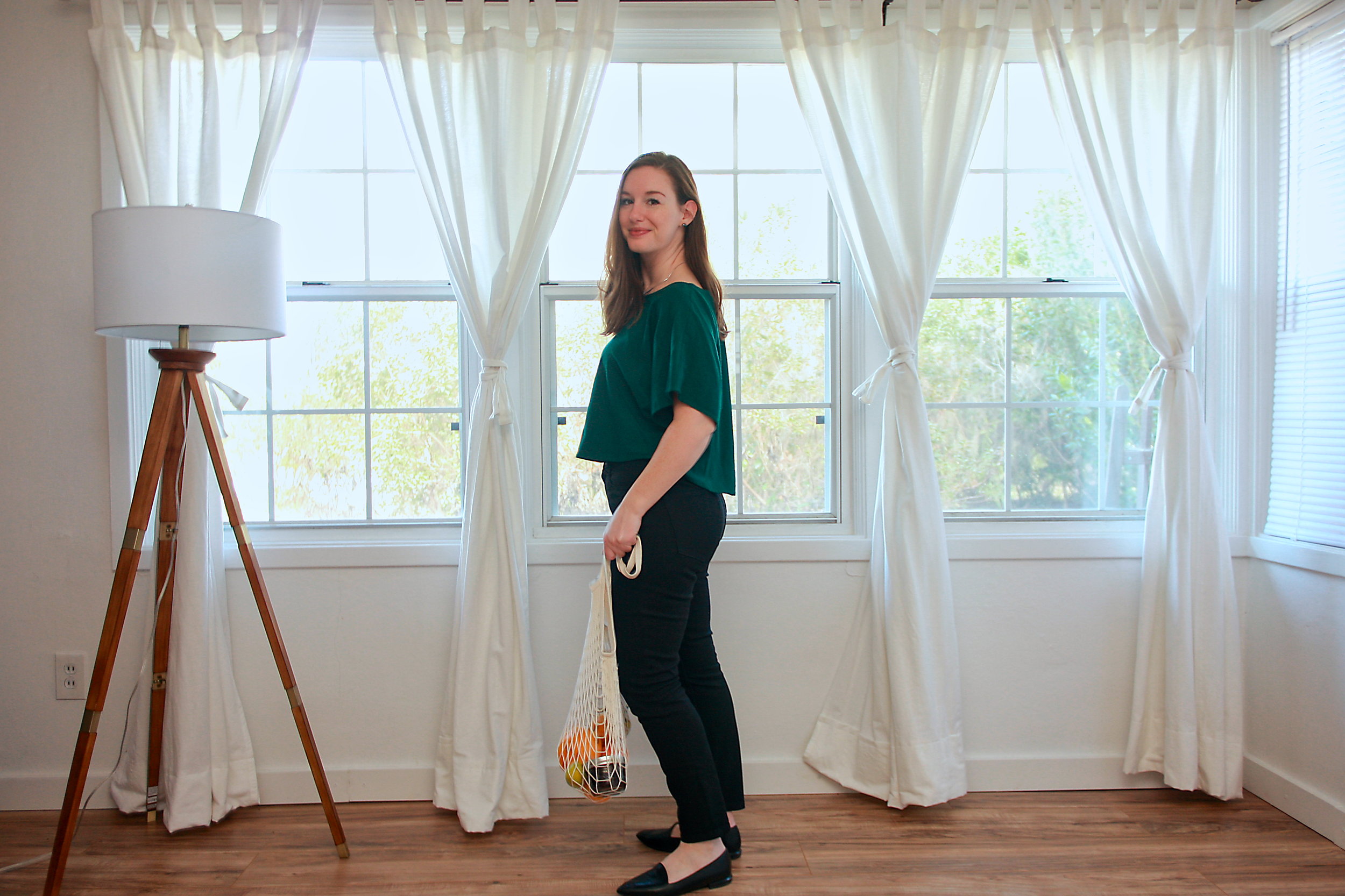 Alyssa wears a green top, black jeans, and black flats while facing sideways