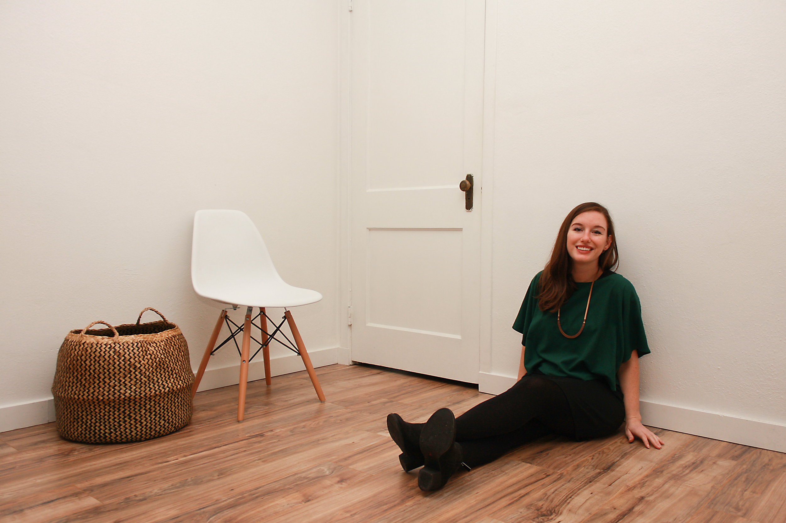 Alyssa wears a green silk top over a black dress with tights and boots while sitting on the floor