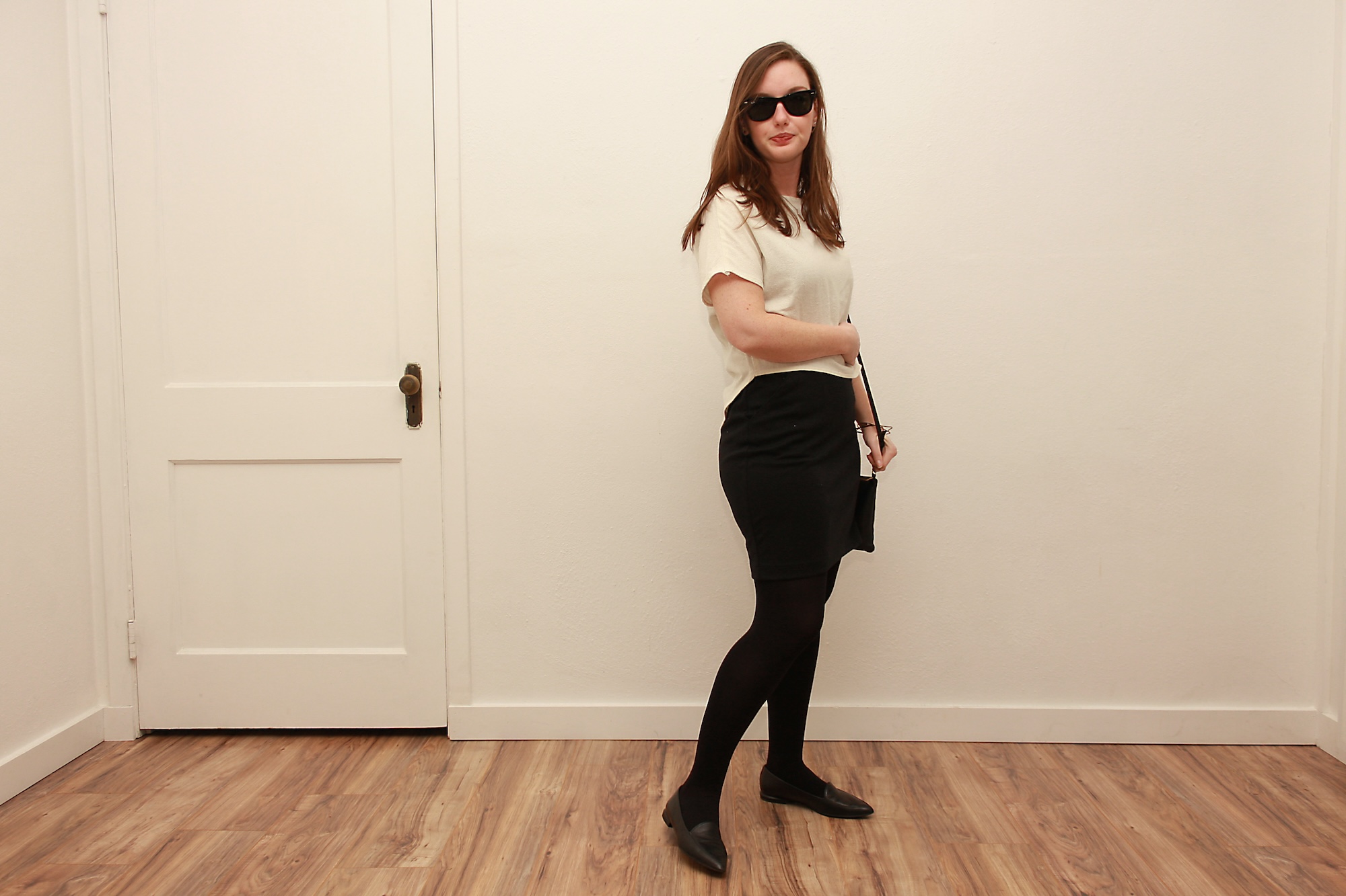  Alyssa wears a white silk tee over a black dress with tights and flats while holding a black purse 