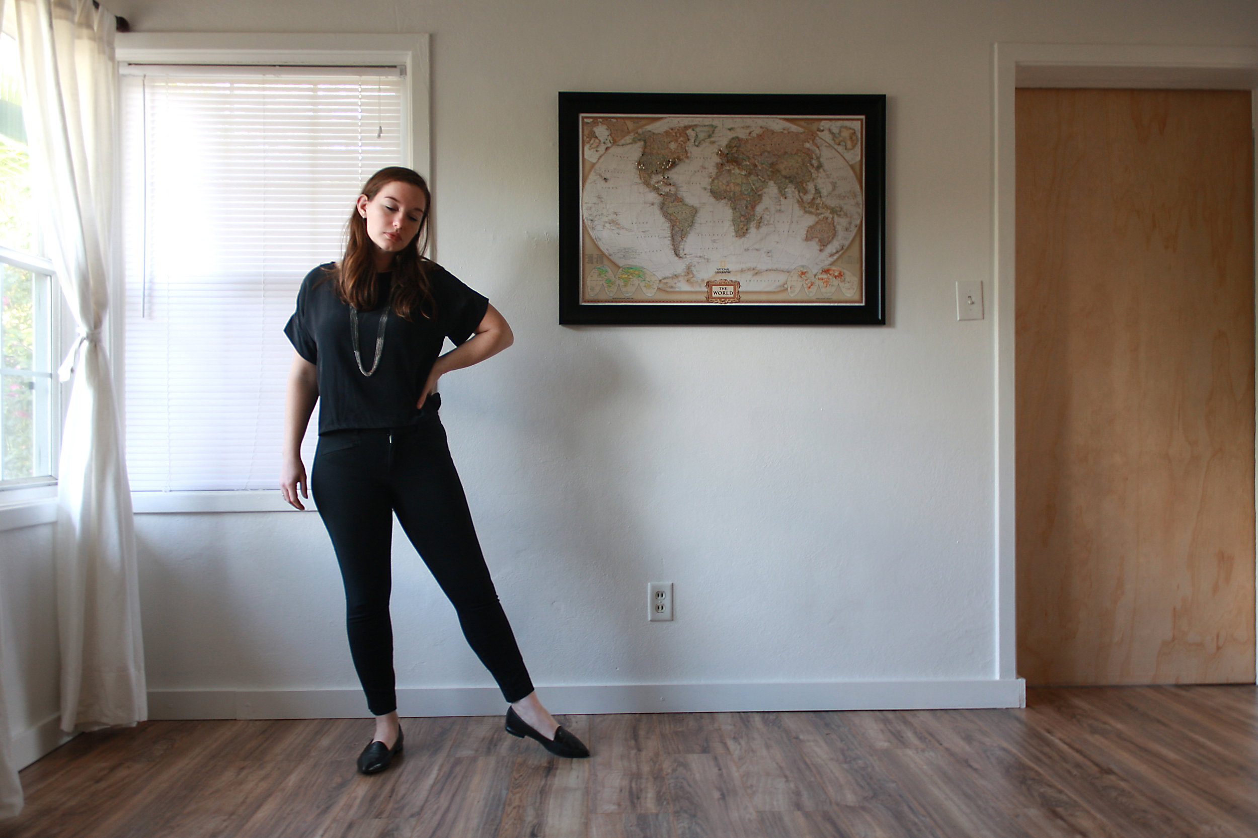 Alyssa wears a silk tee, black pants, and black flats while kicking her leg out to one side