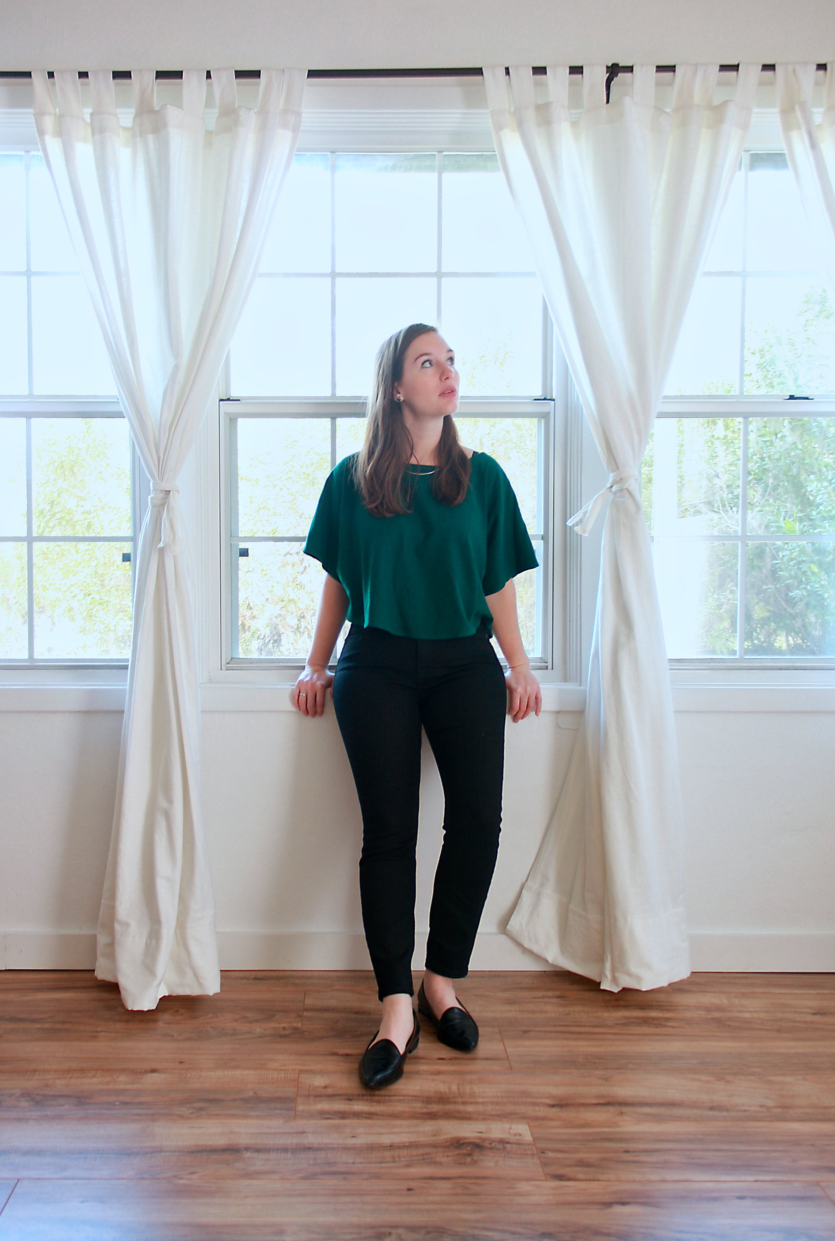 Alyssa wears a green top, black jeans, and black flats while sitting in the window ledge