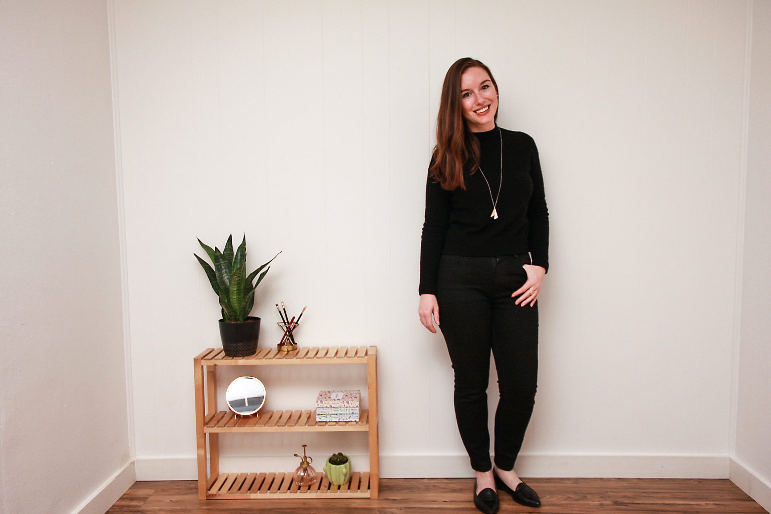 Alyssa wears a black sweater, black jeans, and black flats and smiles at the camera