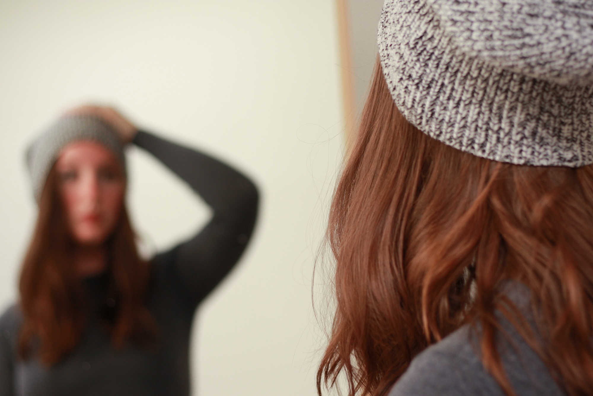 Alyssa adjusts a grey beanie on her head in a mirror