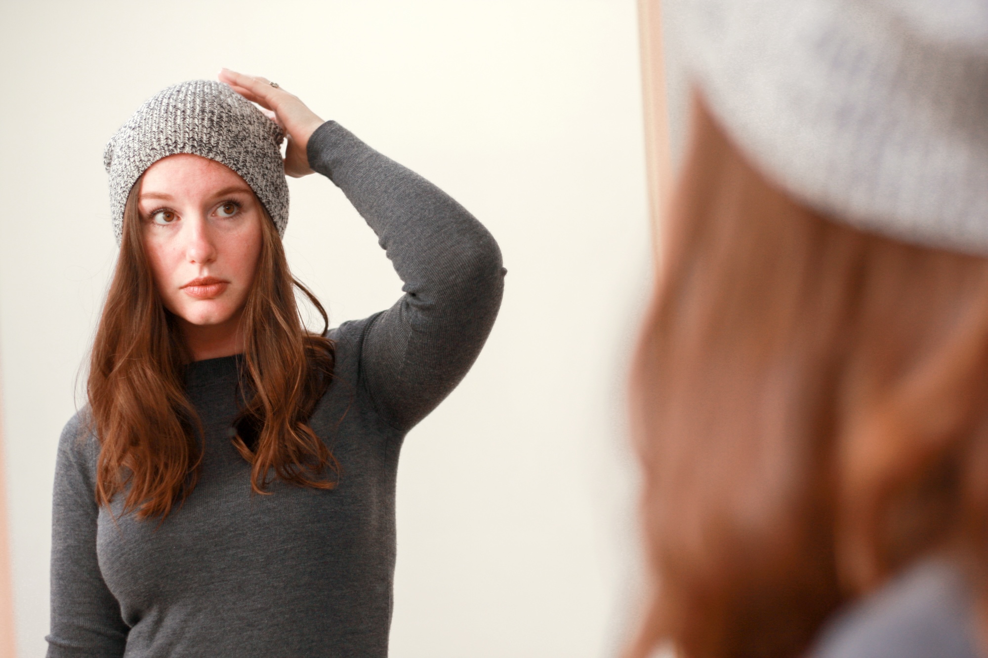 Alyssa adjusts a grey beanie on her head in the mirror