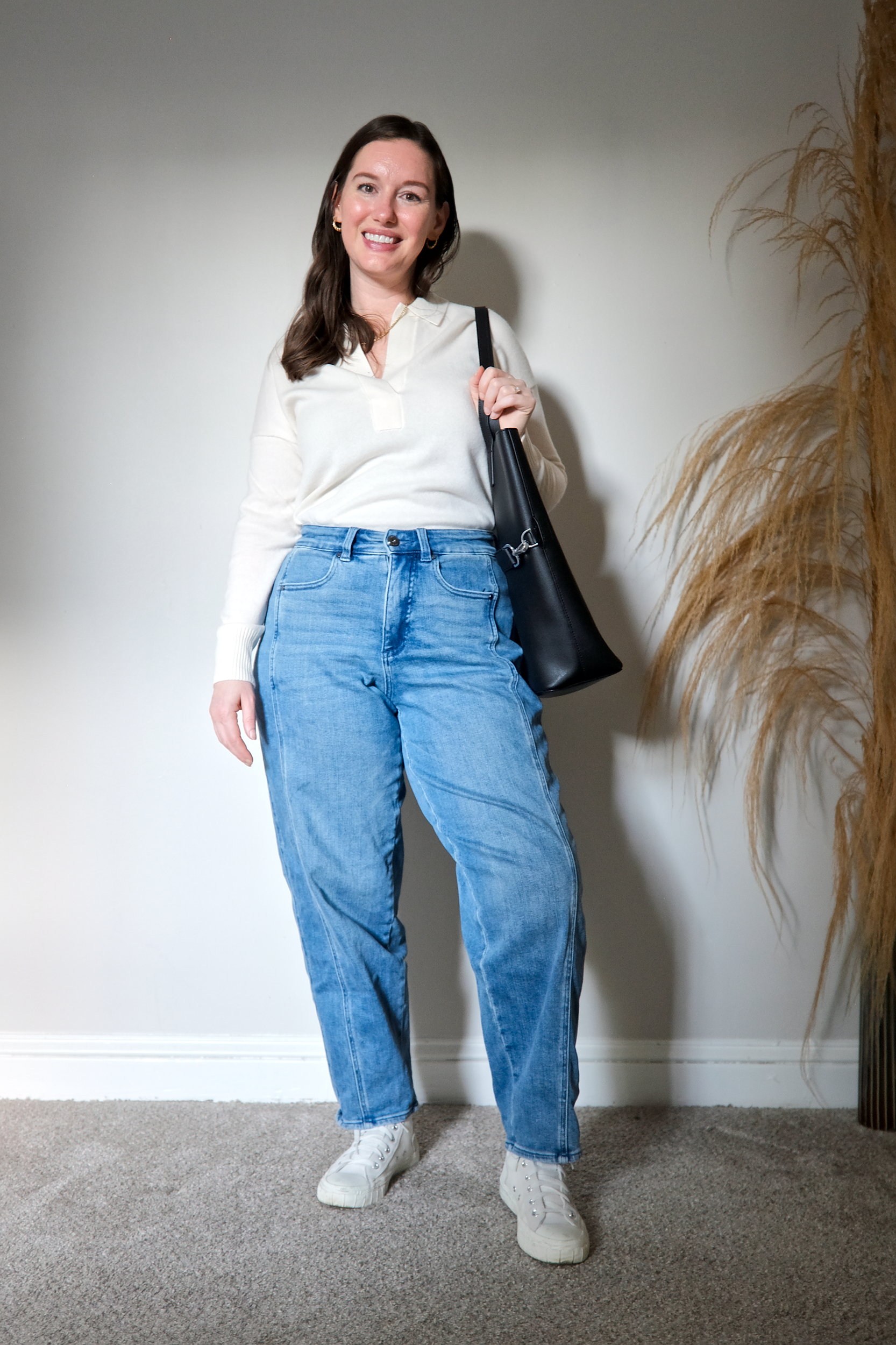 Alyssa wears the ivory cashmere polo sweater tucked into blue jeans with sneakers. She carries a tote and smiles at the camera.