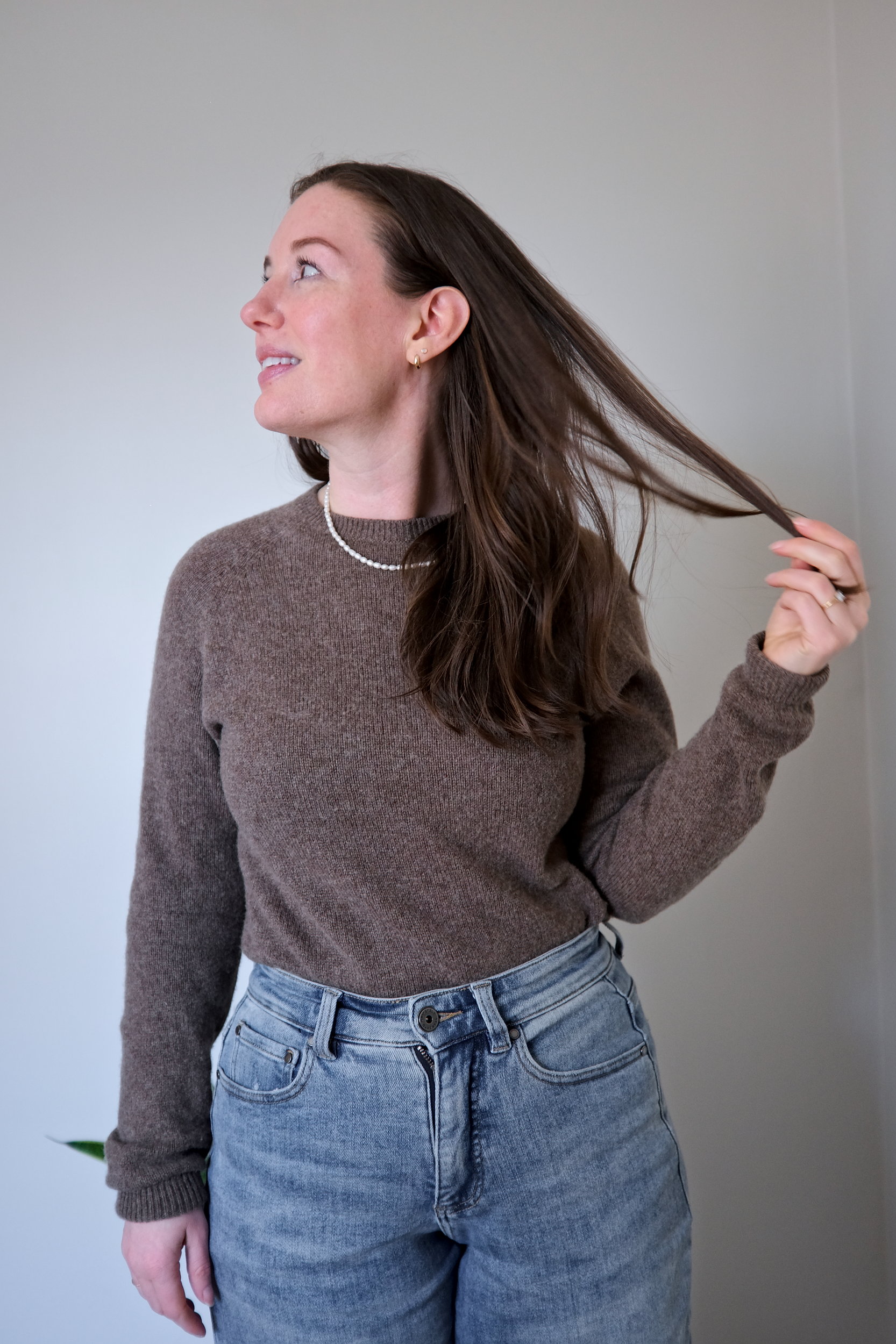 Alyssa wears a yak sweater from Quince in soft brown and plays with her hair in a close-up shot