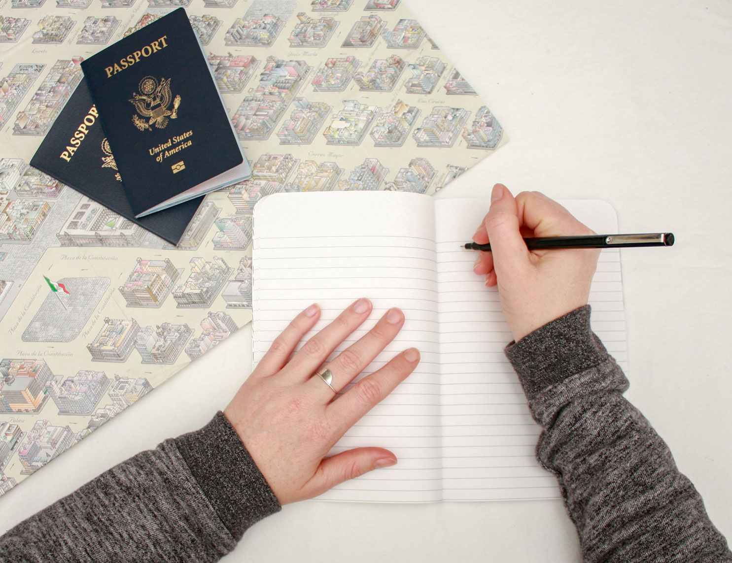 A hand prepares to write in a blank notebook, with a map and passport in the image