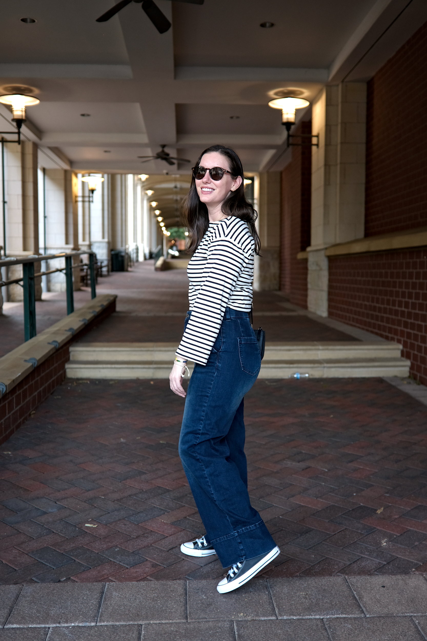 Alyssa wears the Carol High Rise High Stretch Jeans with a striped tee, sneakers, and sunglasses. She faces to the side.