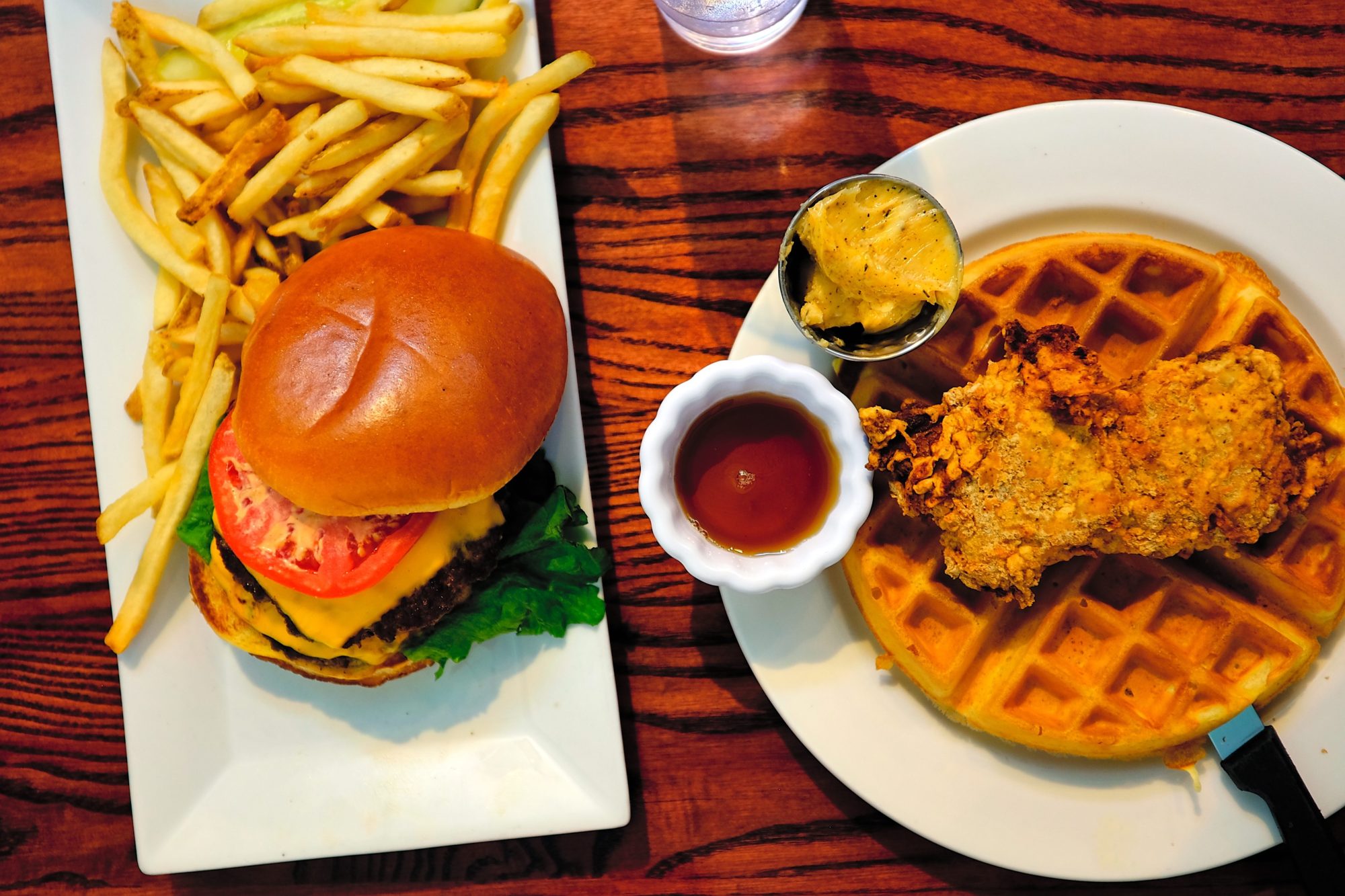 A burger and a plate with chicken and waffles