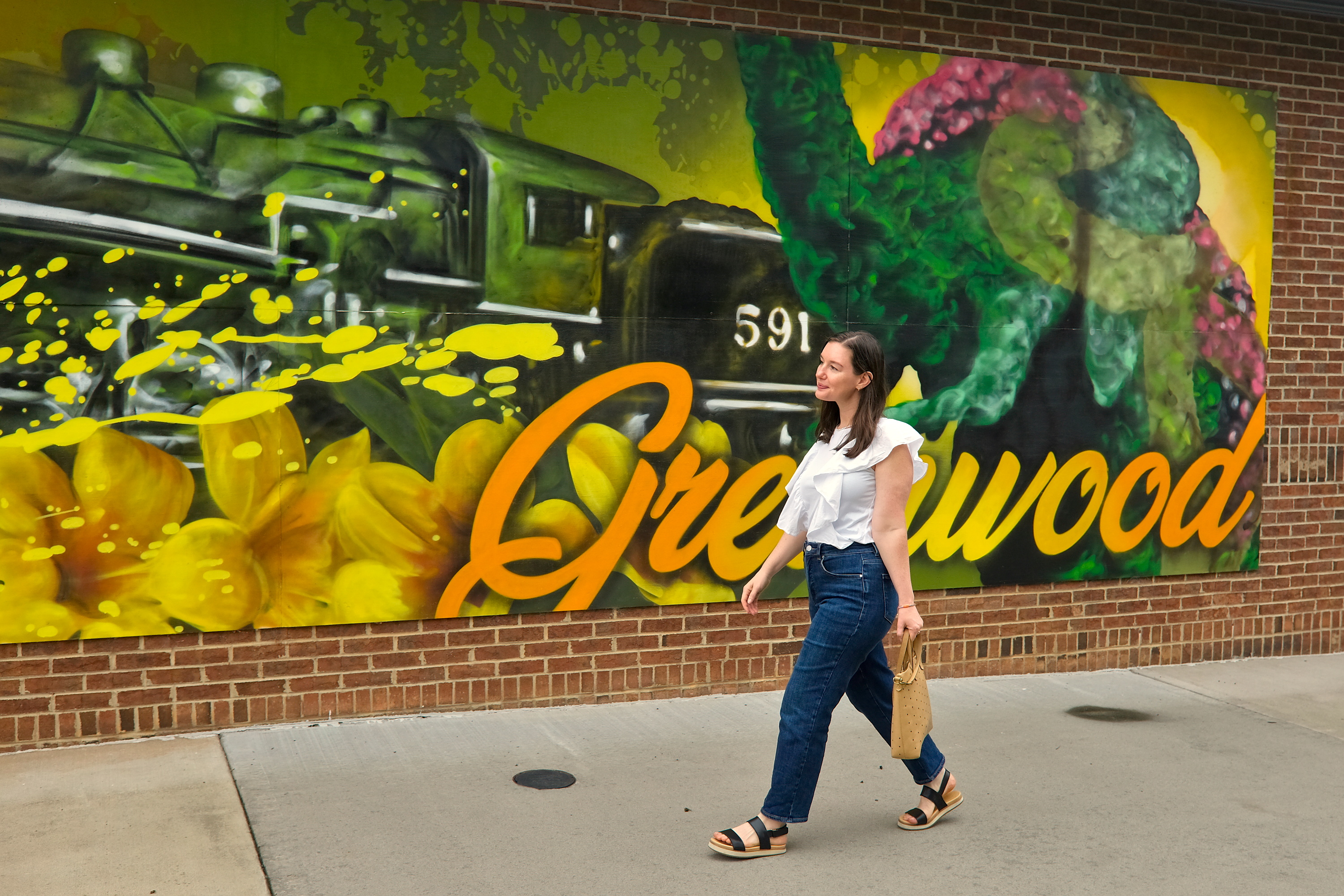 Alyssa walks in front of a mural depicting a train and flowers