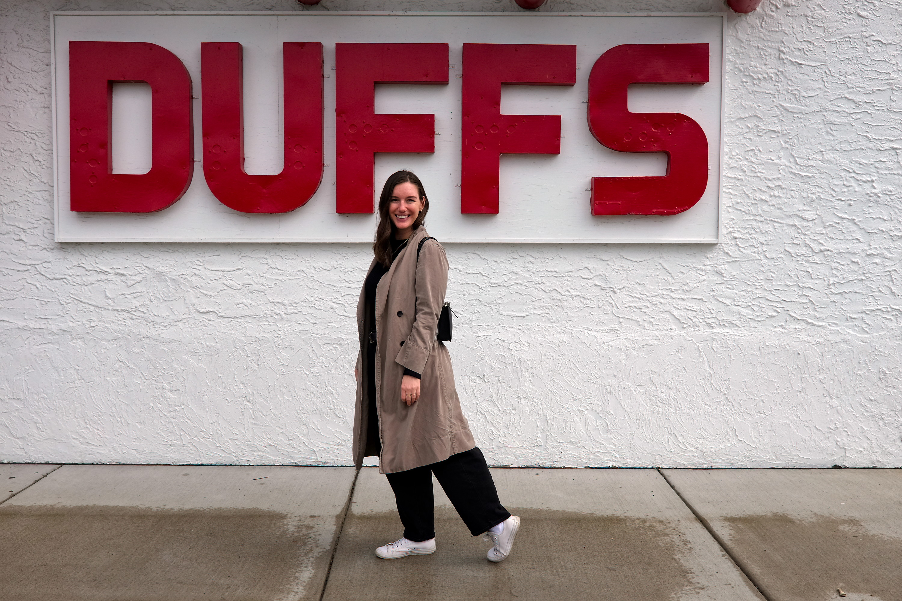 Alyssa wears a black top, jeans, and sneakers in front of Duff's