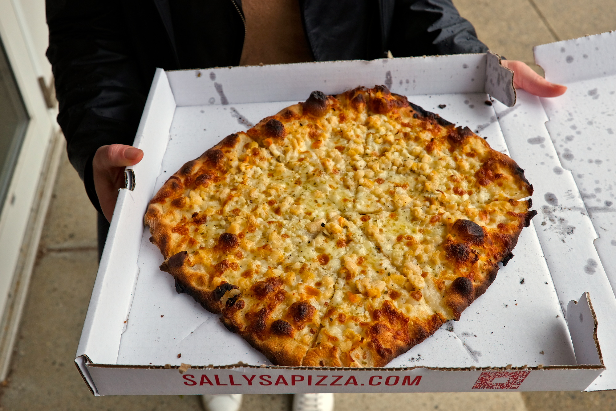 Alyssa holds a pizza from Sally's Apizza