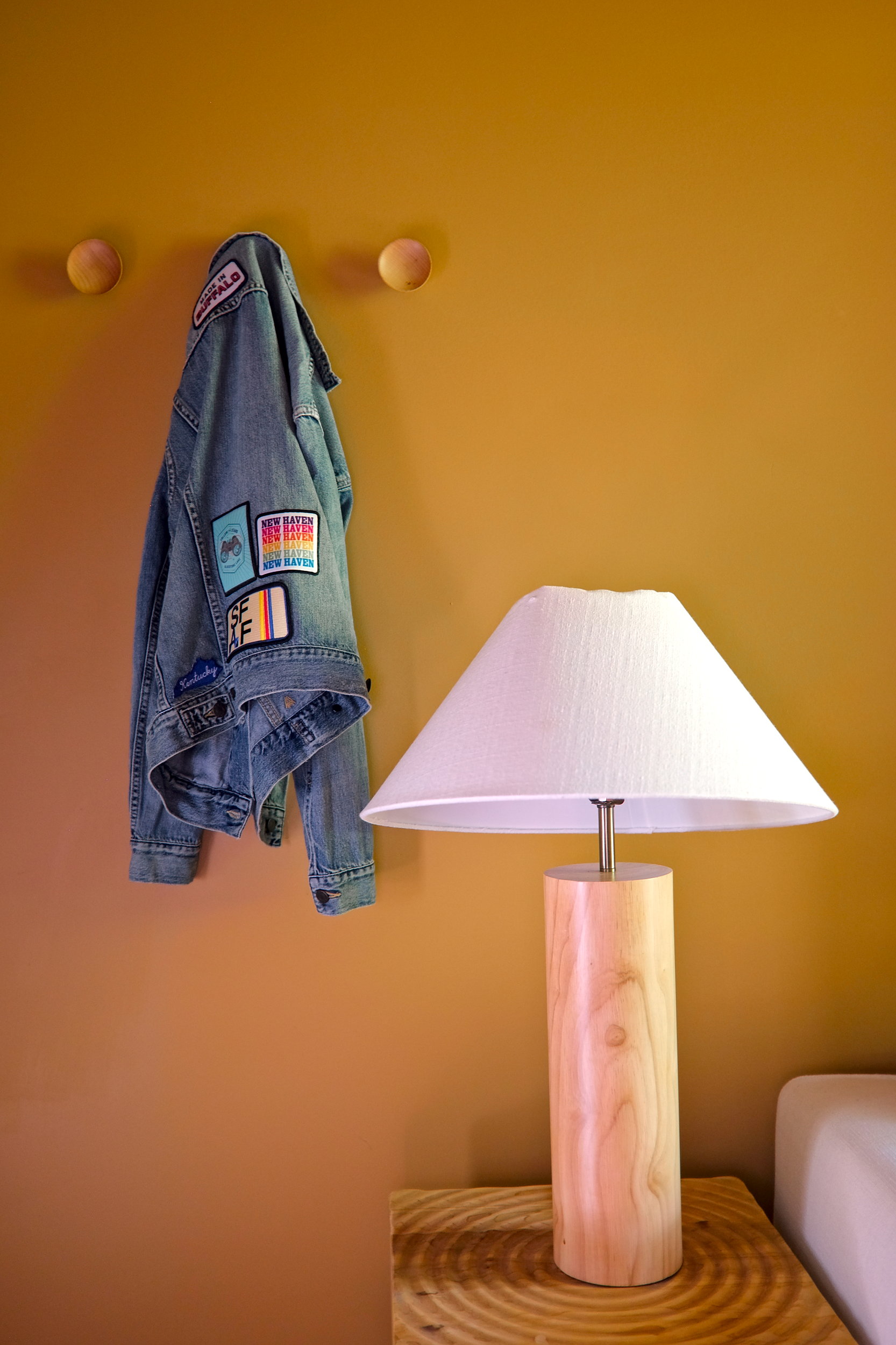 A denim jacket covered in patches hangs on a wall hook