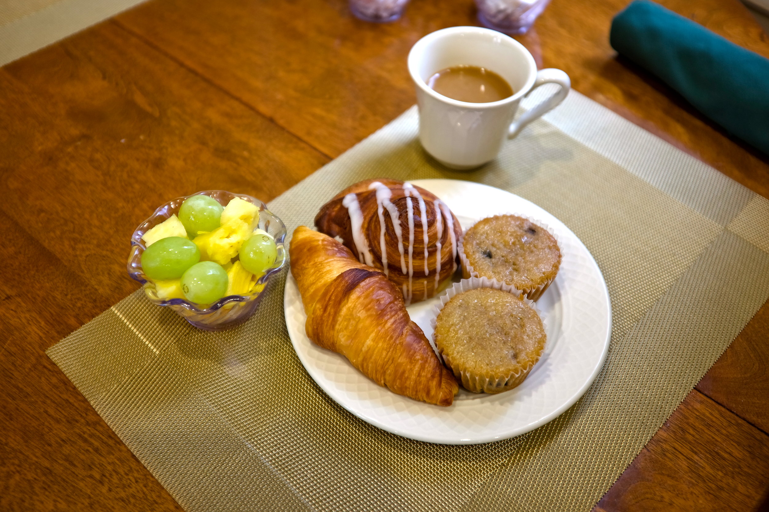 A plate of pastries, cup of coffee, and fruit on a table