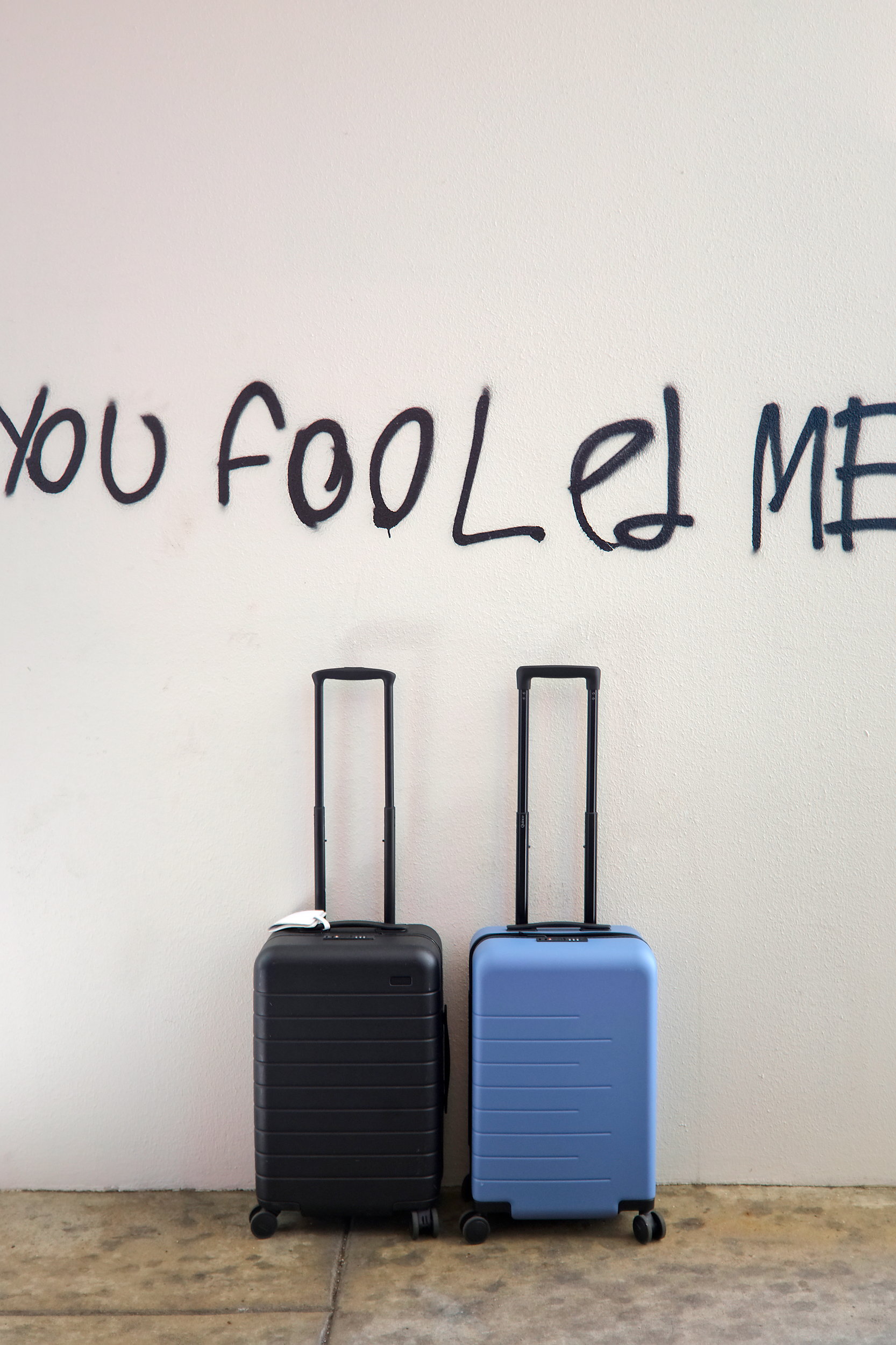 The Quince and Away suitcases sit under graffiti that reads "you fooled me"