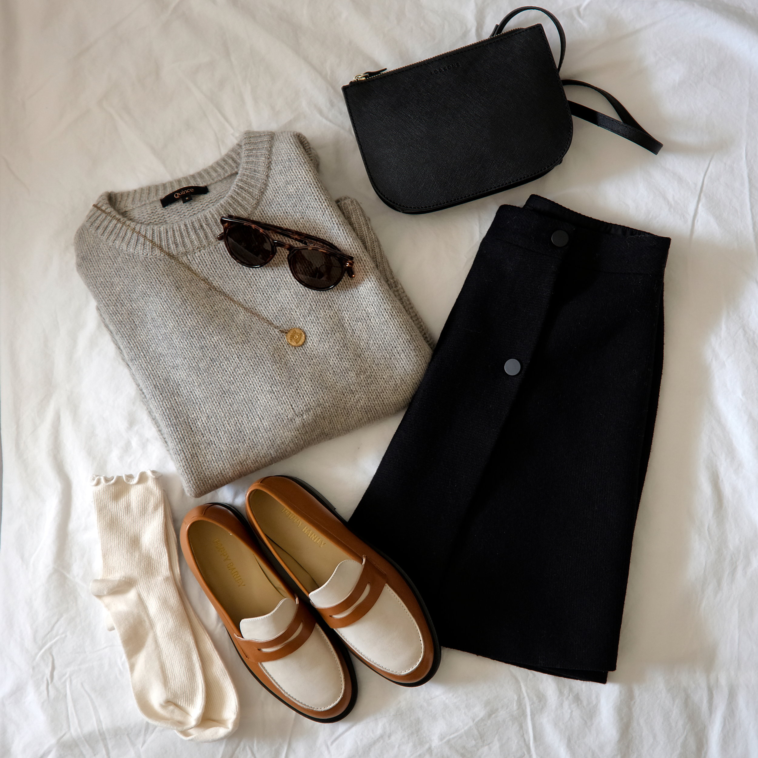 An outfit flatlay with a sweater, skirt, purse, loafers, and socks