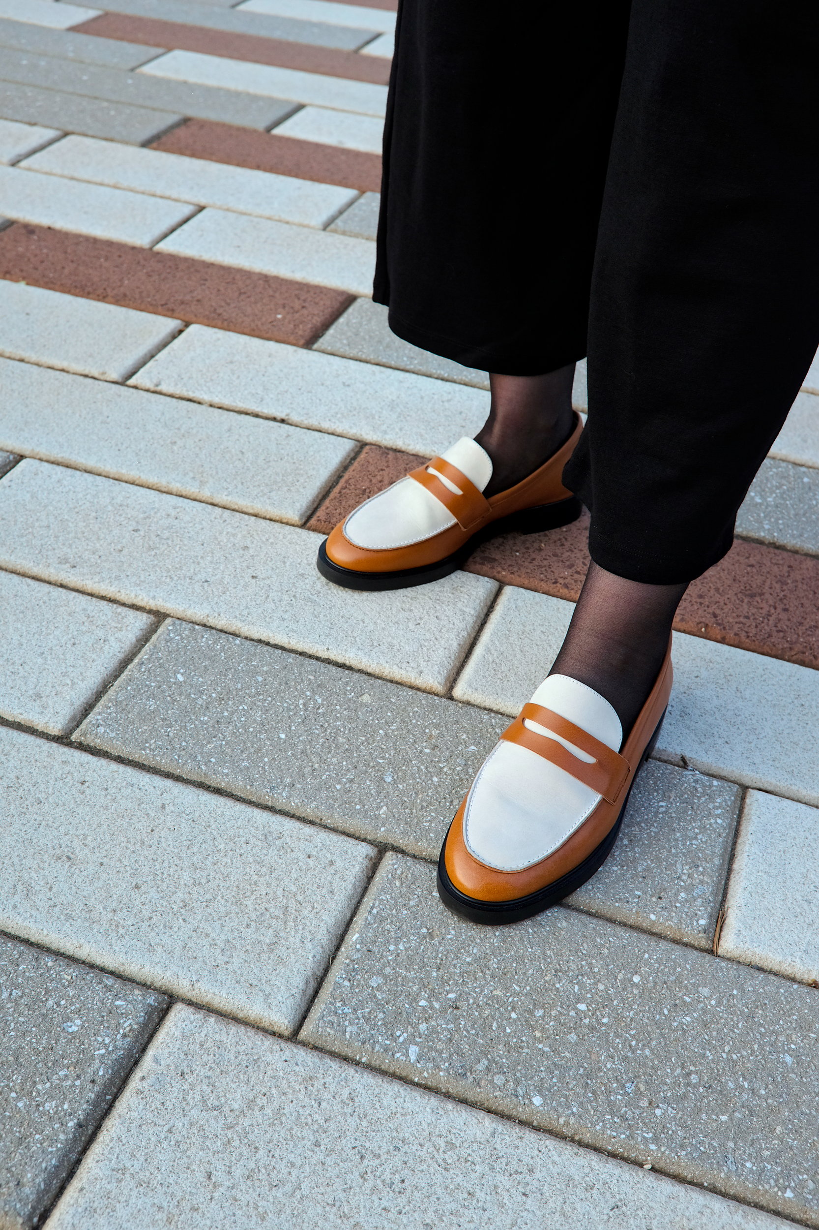 Alyssa wears a pair of loafers on a brick sidewalk