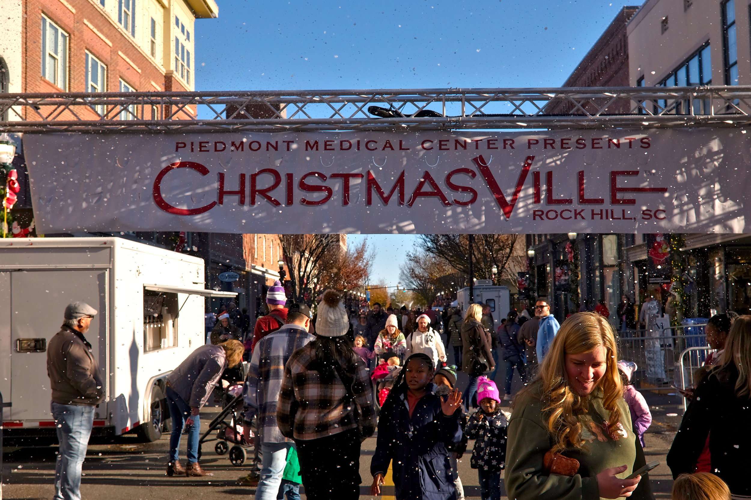 A crowd of people walk under faux snow at ChristmasVille in Rock Hill