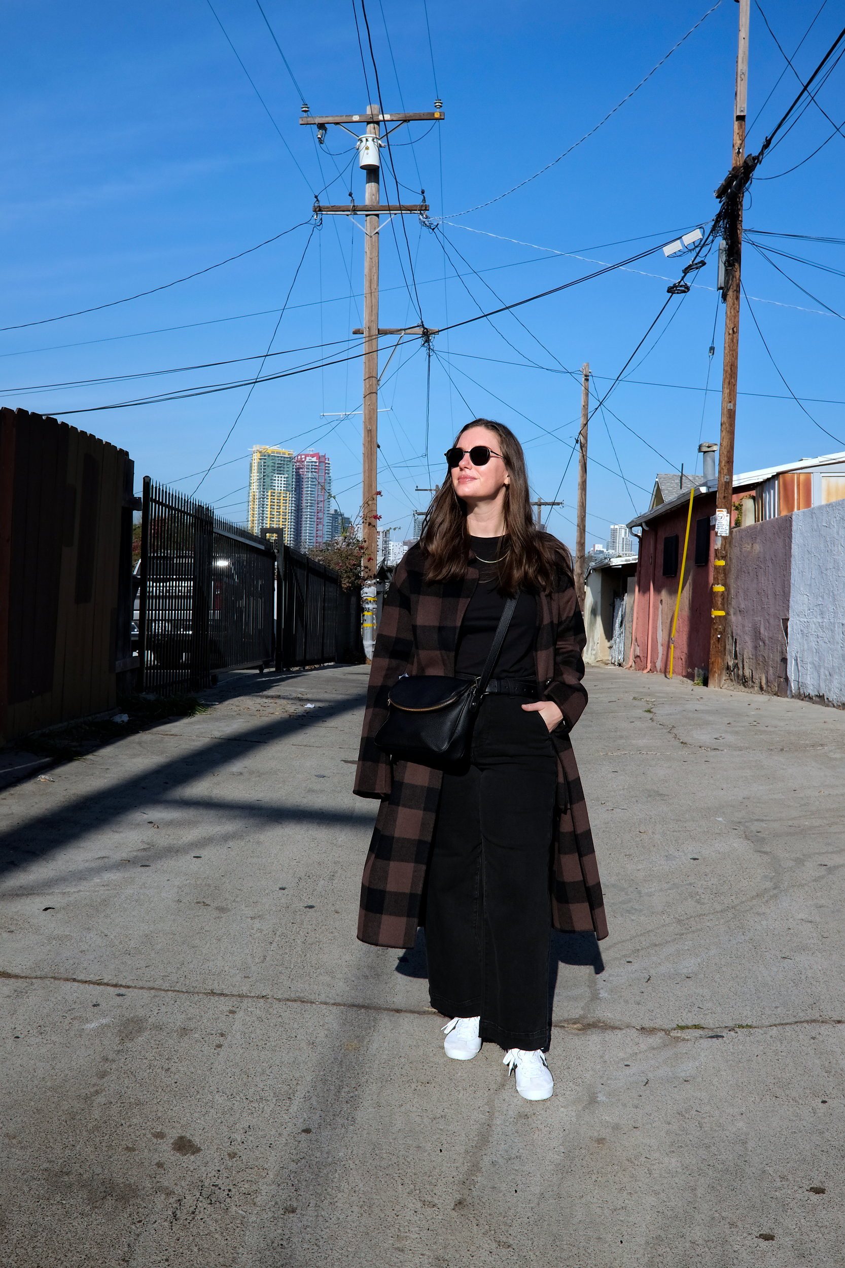 Alyssa walks down a street in San Diego in a coat, black top, and black jeans