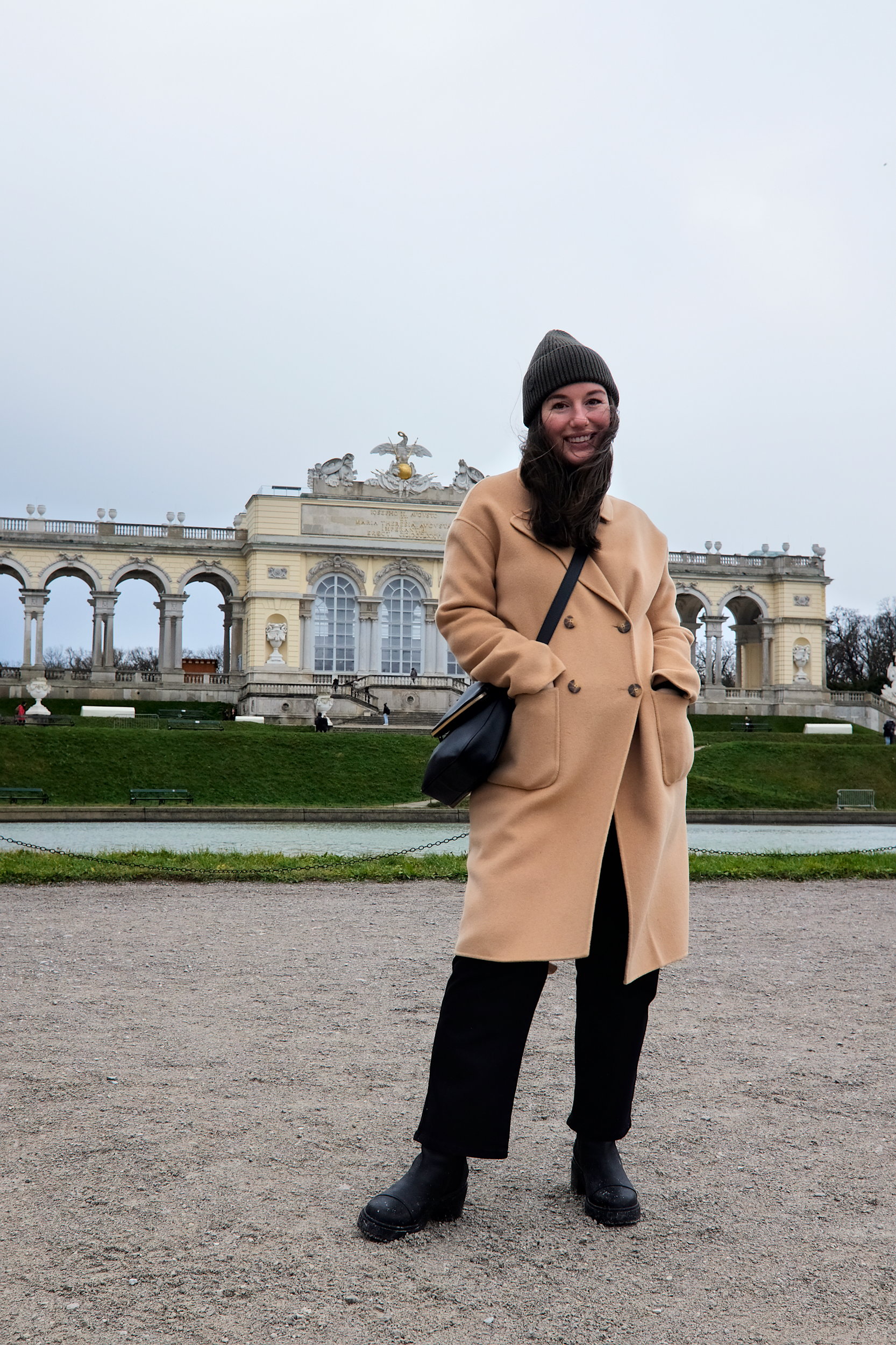 Alyssa at the Gloriette in Vienna, wearing a camel coat, beanie, and boots