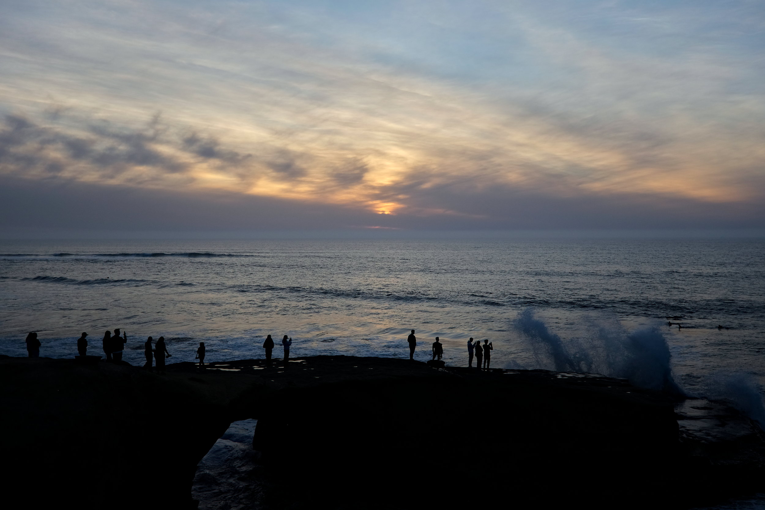 A crowd watches the sun set behind clouds at 