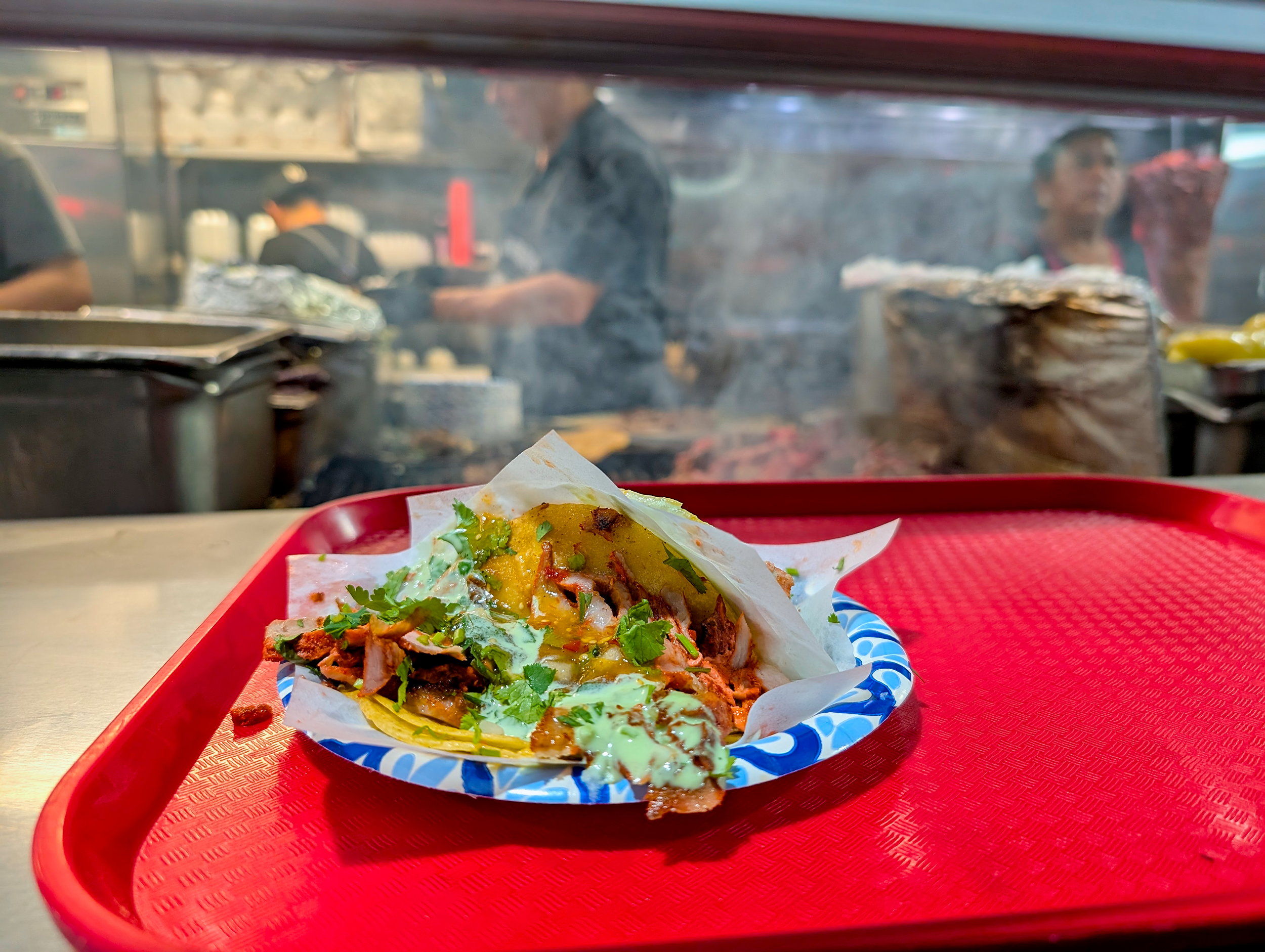 A taco on a tray with cooks in the background