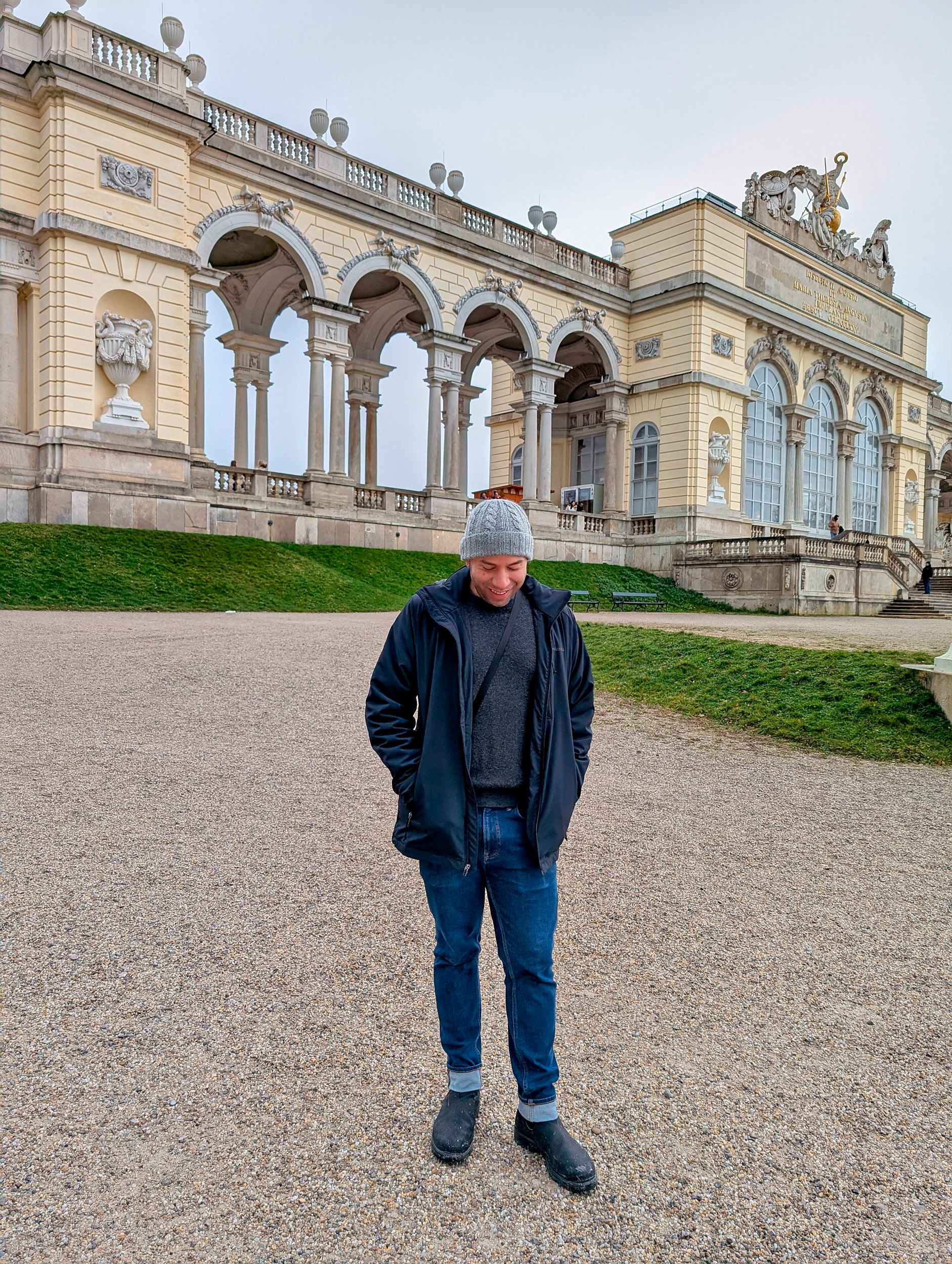 Michael wears a grey sweater, jeans, and a jacket at Gloriette in Vienna