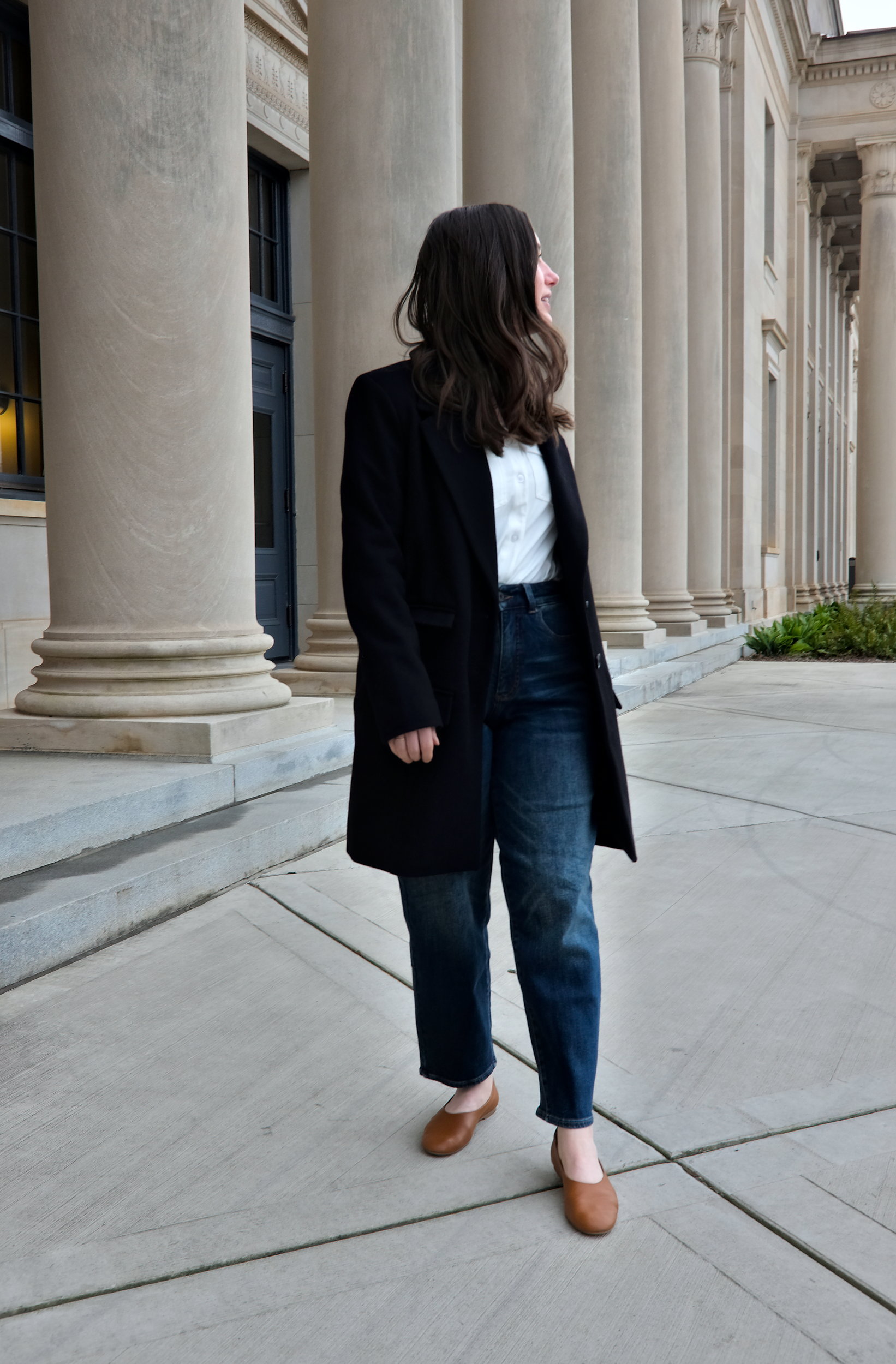 Alyssa wears a black wool coat from Universal Standard with a white top and brown shoes