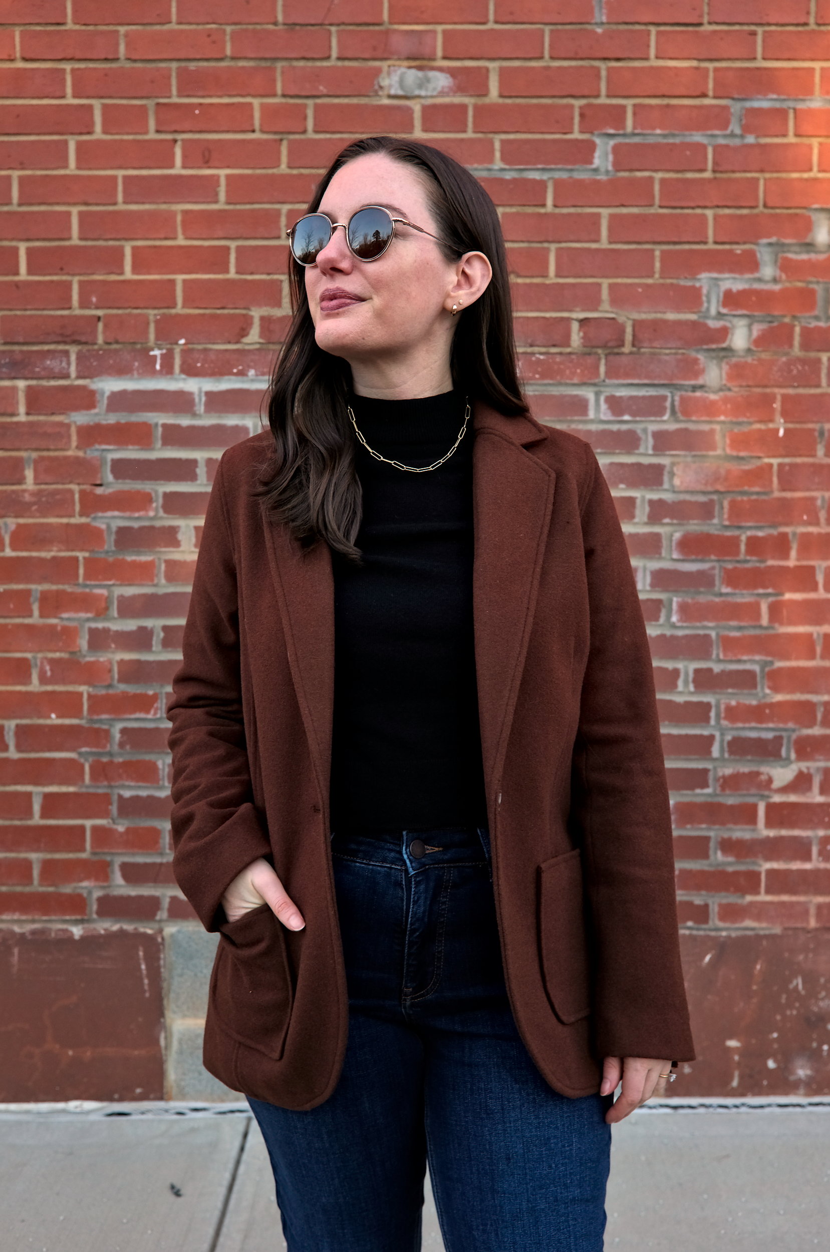 Alyssa wears the Kidjo Tailored Wool Jacket, a brown wool coat from Universal Standard, along with blue jeans and a black sweater